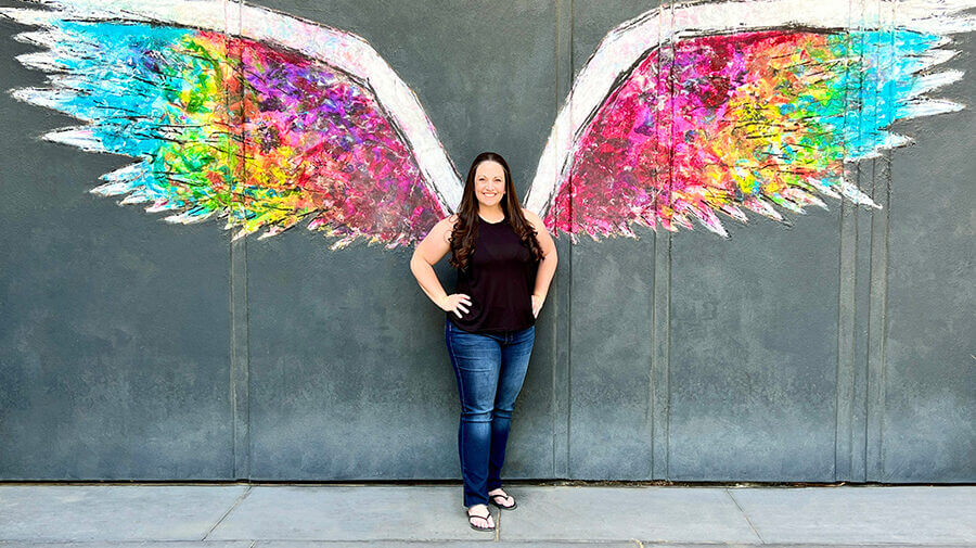 Jennifer Bourn standing in front of painted rainbow wings