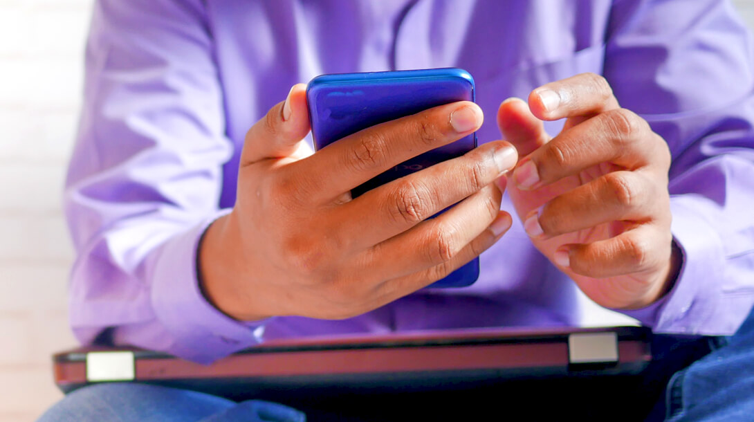 A man in a purple shirt engaging in content marketing for his small business on his smartphone