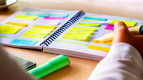 woman planning weekly to-dos in a planner using colorful sticky notes