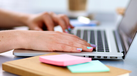 A woman with colorful painted nails working on a laptop to complete a DIY branding and business course
