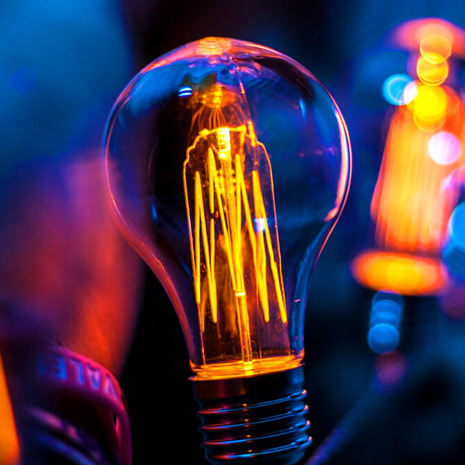 A bright lightbulb in pinks and opranges on a dark navy blue background to represent freelancer pricing ideas