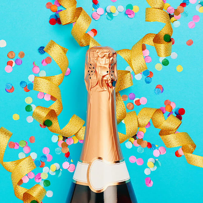 A bottle of champagne, rainbow confetti, and curly gold ribbon to celebrate freelancer pricing success
