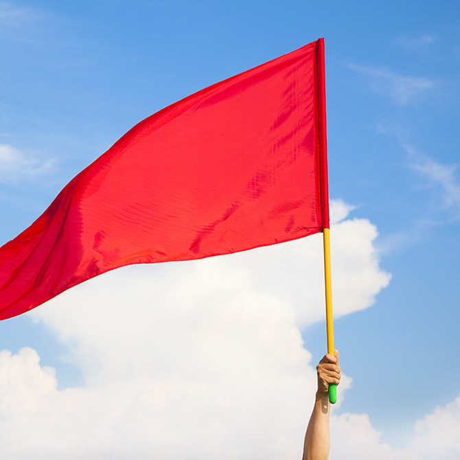 A bright red flag being raised in the air against a blue sky to offer a red flag warning