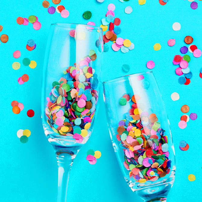 Two champagne flutes full of paper confetti, in a bright turquoise background, with confetti sprinkled around the glasses to celebrate fit for the Client Conflict Cure