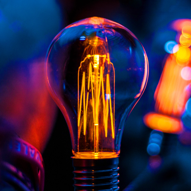 A bright lightbulb in pinks and opranges on a dark navy blue background to represent freelancer pricing ideas