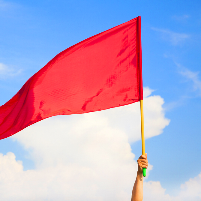 A bright red flag being raised in the air against a blue sky to offer a red flag warning